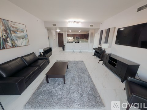 A living room with a black leather couch and a grey rug.