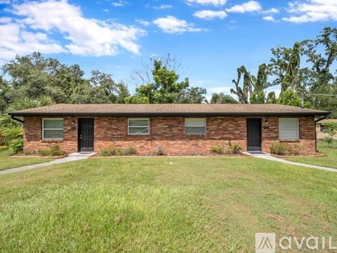 A brick house with a grassy front yard and trees in the background.