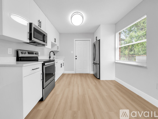 A modern kitchen with white cabinets and appliances, a wooden floor, and a window with a view of trees outside.