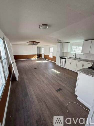 A spacious kitchen and living room with white cabinets and a brown floor.