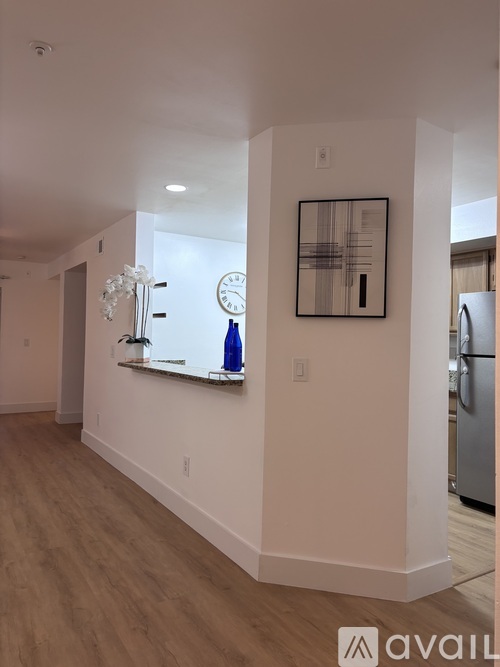 A modern kitchen with a refrigerator, a clock, and a painting on the wall.