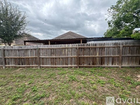 A wooden fence surrounds a grassy area with a house in the background.