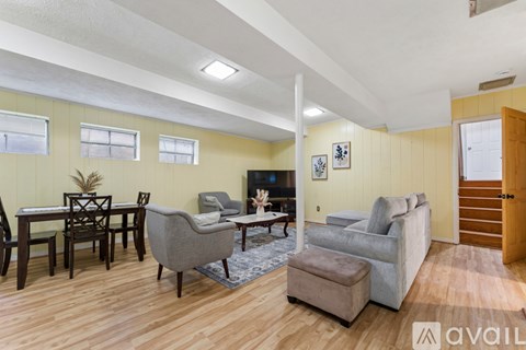 A living room with a grey couch, a brown ottoman, a wooden dining table and chairs, and a television.