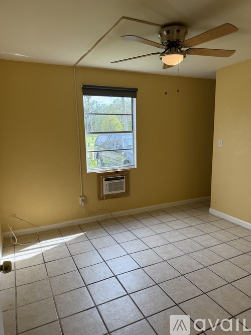A room with yellow walls, a ceiling fan, and a window with a view of a parking lot.