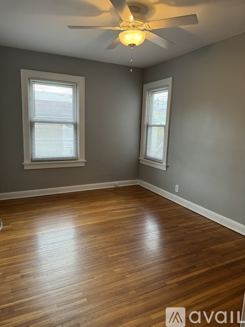 A room with wooden flooring and two windows.