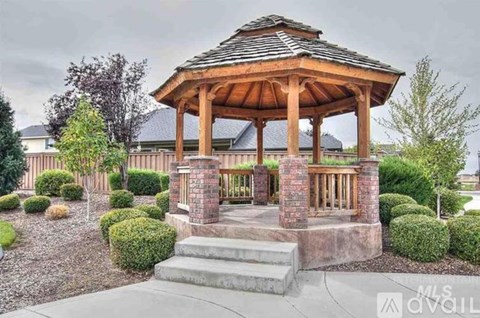 A gazebo with a brown roof is surrounded by bushes and trees.