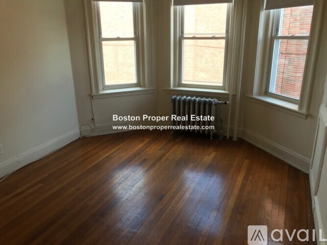 A room with wooden flooring and two windows.