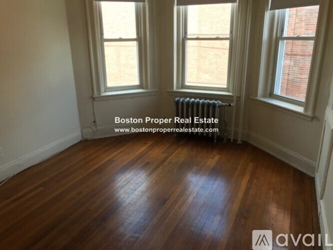 A room with wooden flooring and two windows.