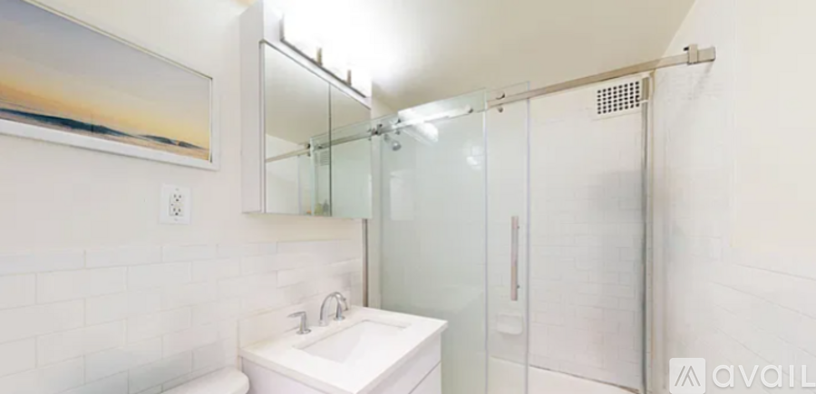 A white sink in a white tiled bathroom with a glass shower door.