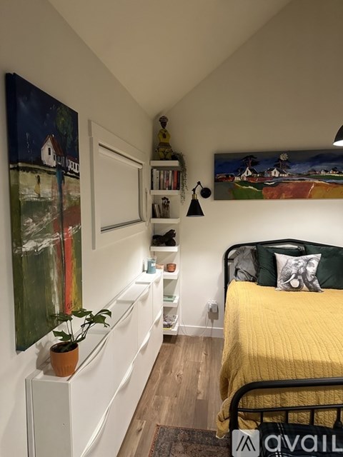 A bedroom with a bed, a shelf with a plant on it, and two paintings on the wall.