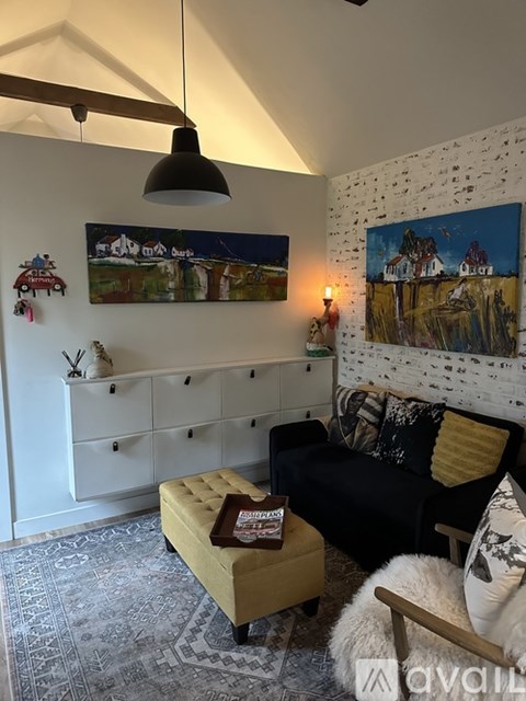 A living room with a black couch, a yellow ottoman, and a painting on the wall.