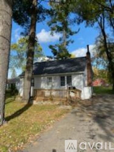 A small white house with a black roof is surrounded by trees.