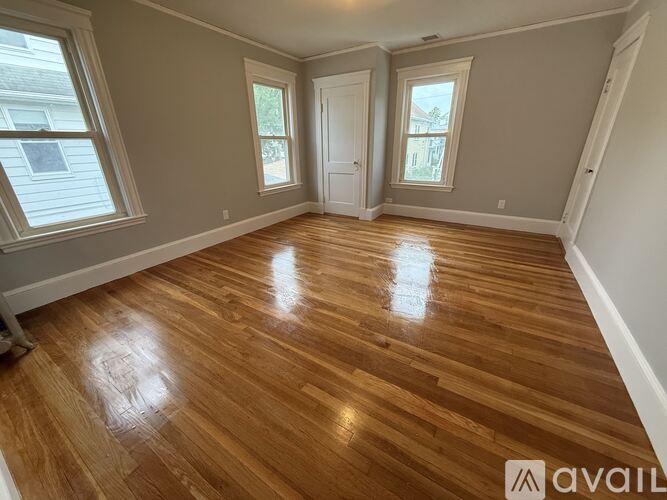 A room with wooden flooring and three windows.