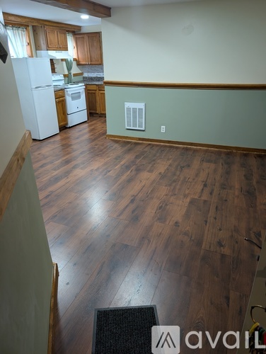 A room with wooden floors and a kitchen area in the background.