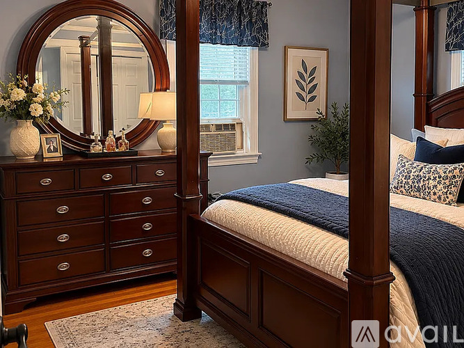 A bedroom with a large bed, a dresser with a mirror, and a window with a plant.