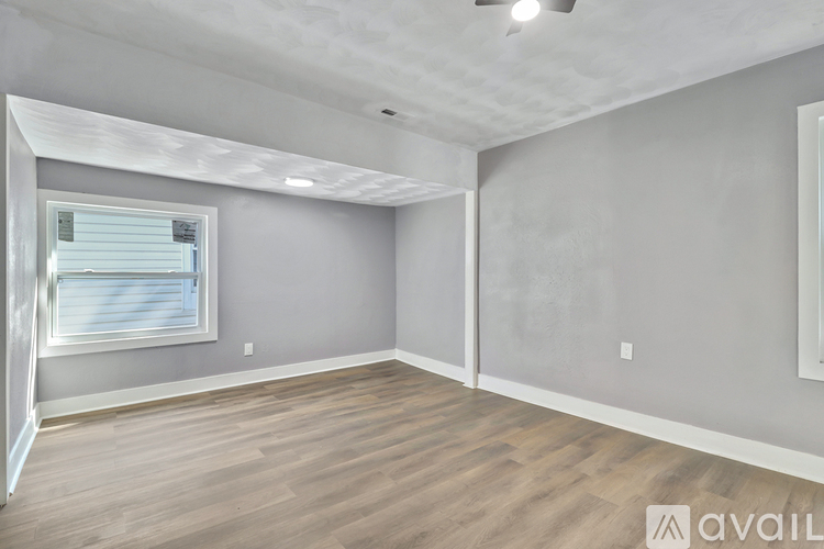 A spacious room with wooden flooring and a window with blinds.