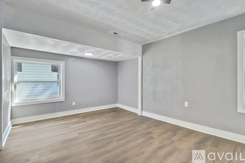 A spacious room with wooden flooring and a window with blinds.