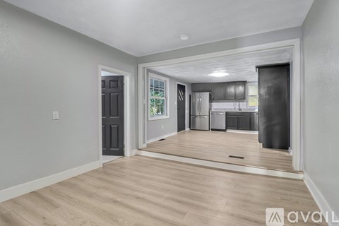 A spacious room with wooden flooring and a kitchen area in the background.
