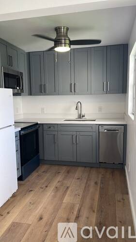A kitchen with a white fridge, a black oven, a white sink and a ceiling fan.