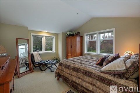 A bedroom with a bed, chair, and two windows.