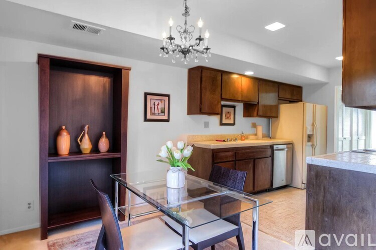 A modern kitchen with a glass table and chairs, a chandelier, and a cabinet with a wooden door.