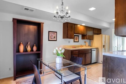 A modern kitchen with a glass table and chairs, a chandelier, and a cabinet with a wooden door.