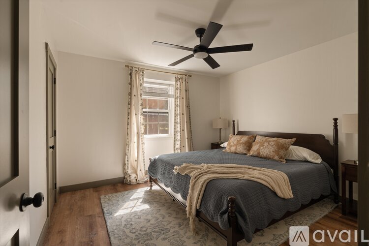 A bedroom with a bed, a ceiling fan, and a window with curtains.