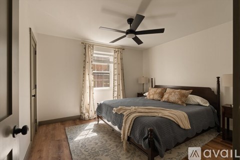 A bedroom with a bed, a ceiling fan, and a window with curtains.