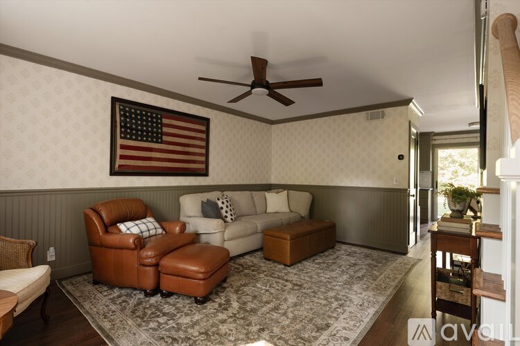 A living room with a brown leather chair and ottoman, a white couch, and an American flag hanging on the wall.