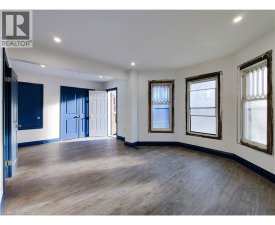 A spacious room with wooden floors and three windows.