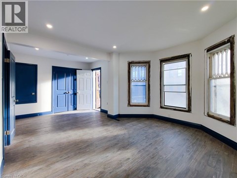 A spacious room with wooden floors and three windows.