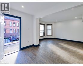 A room with wooden floors and white walls, with a view of a red building outside through a glass door.