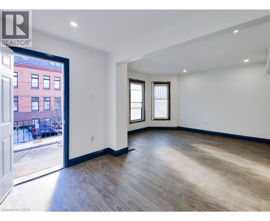 A room with wooden floors and white walls, with a view of a red building outside through a glass door.
