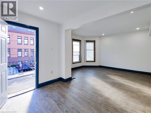 A room with wooden floors and white walls, with a view of a red building outside through a glass door.