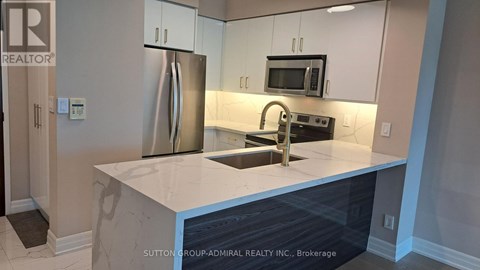 A kitchen with a refrigerator, microwave, and sink.