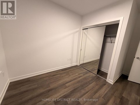 A room with a wooden floor and a white wall with a doorway leading to another room.