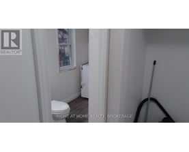 A white toilet in a small bathroom with a REALTOR® logo on the wall.