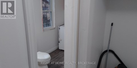 A white toilet in a small bathroom with a REALTOR® logo on the wall.