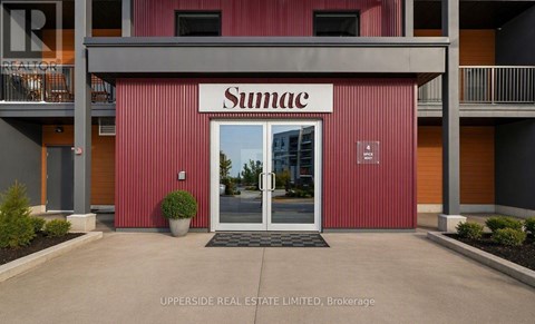 The entrance to a Sumac building with a glass door and a planter in front.