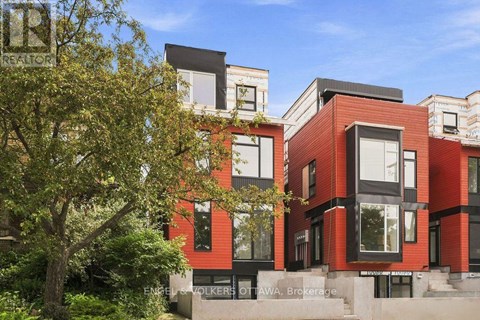 A modern red brick building with black windows and a tree in front.