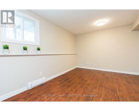 A room with wooden flooring and a window with three potted plants on the windowsill.
