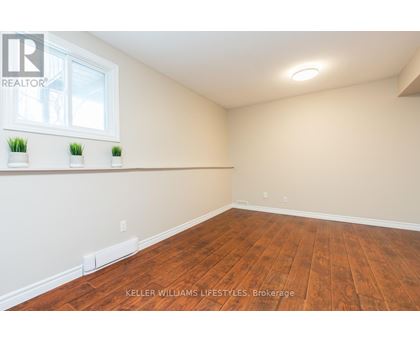 A room with wooden flooring and a window with three potted plants on the windowsill.