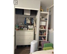 A white closet with clothes hanging and a bookshelf with books.