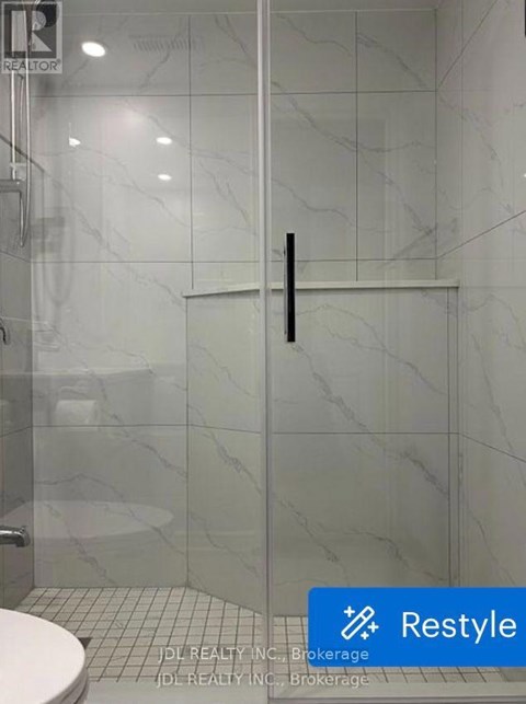 A white toilet sits in a bathroom with a marble wall and a glass door.