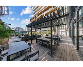 A wooden deck with tables and chairs is surrounded by buildings.