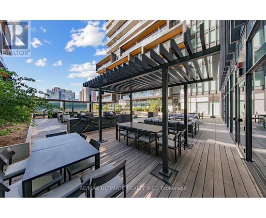 A wooden deck with tables and chairs is surrounded by buildings.