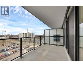 A balcony with glass railings overlooks a parking lot and buildings.