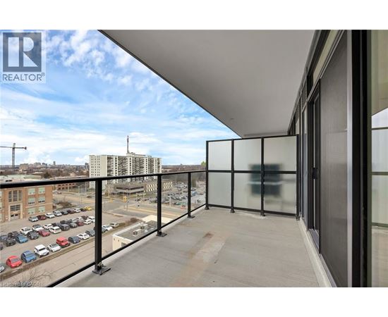 A balcony with glass railings overlooks a parking lot and buildings.