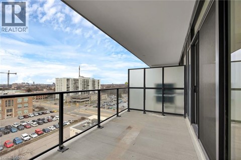 A balcony with glass railings overlooks a parking lot and buildings.