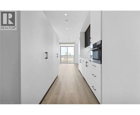 A long, narrow, white hallway with a kitchen area at the end.